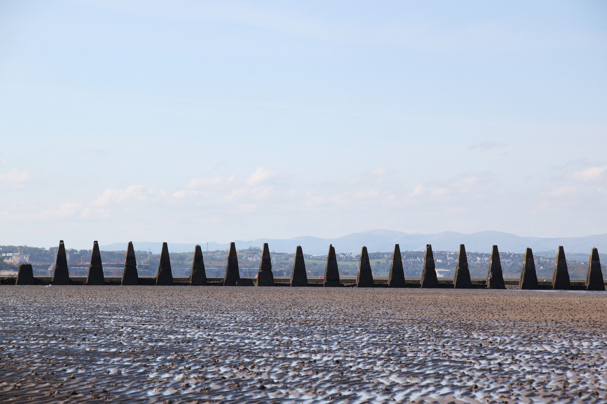 A line of concrete anti-boat pylons crossing the wet sand at Cramond, Edinburgh
