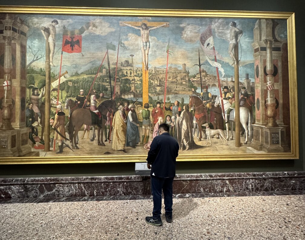 Me, small, standing in front of a wall-sized Renaissance crucifixion in a Milan gallery, reading the label