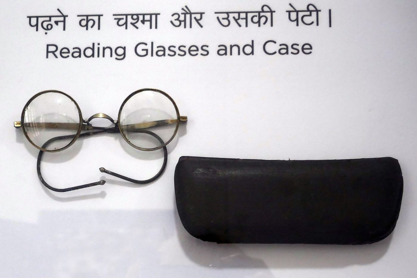Gandhi's round wire reading glasses and black case on display, under a sign in Hindi and English reading Reading Glasses and Case