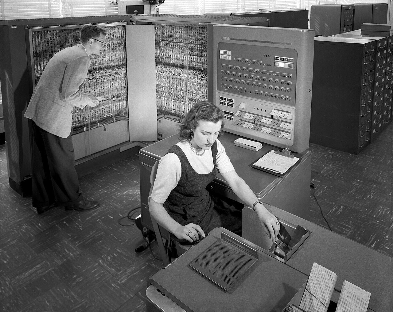 An IBM 704 computer room, with operators at the console and tape drives