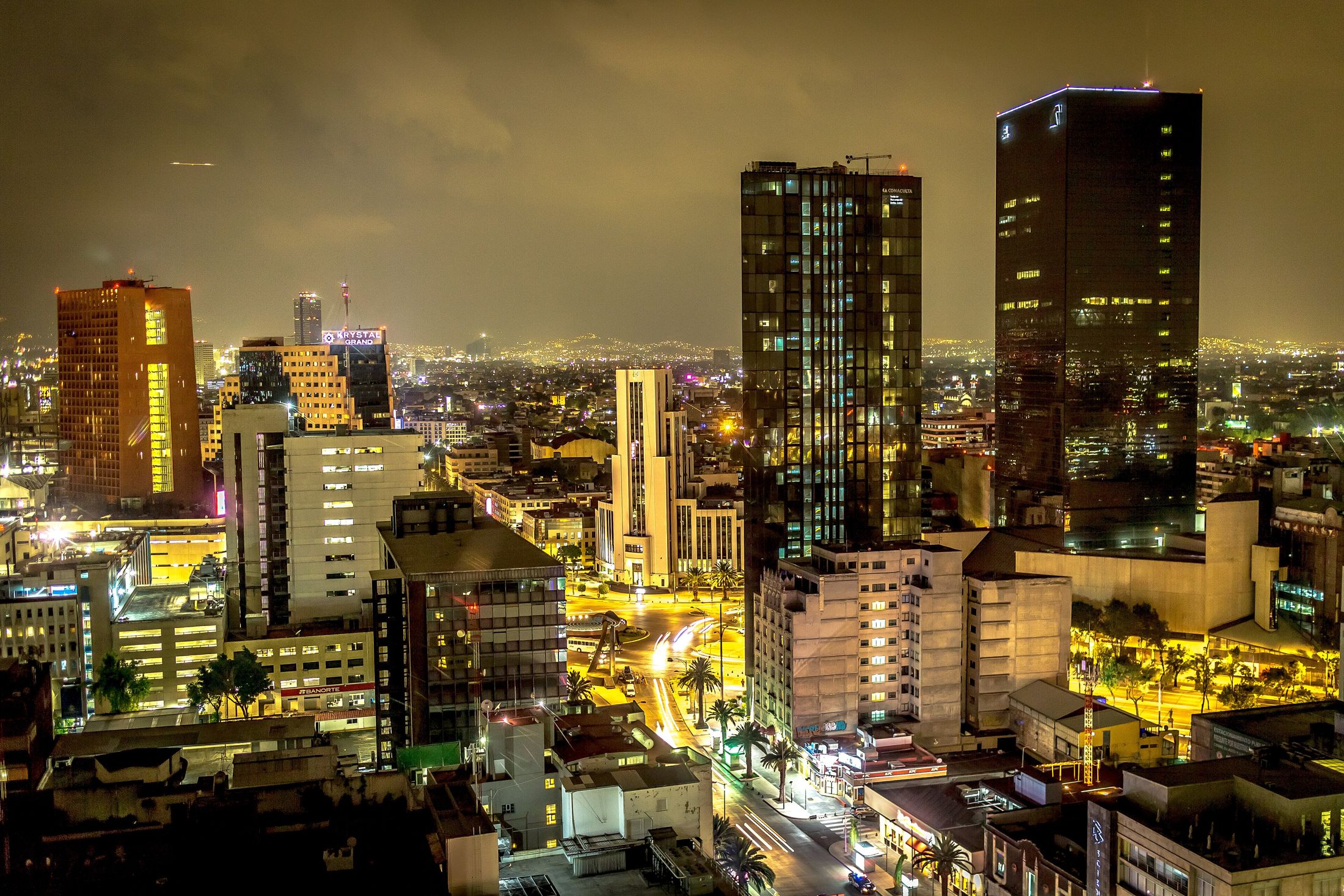 Mexico City at night from above, towers and streets lit orange and white under a hazy, starless sky