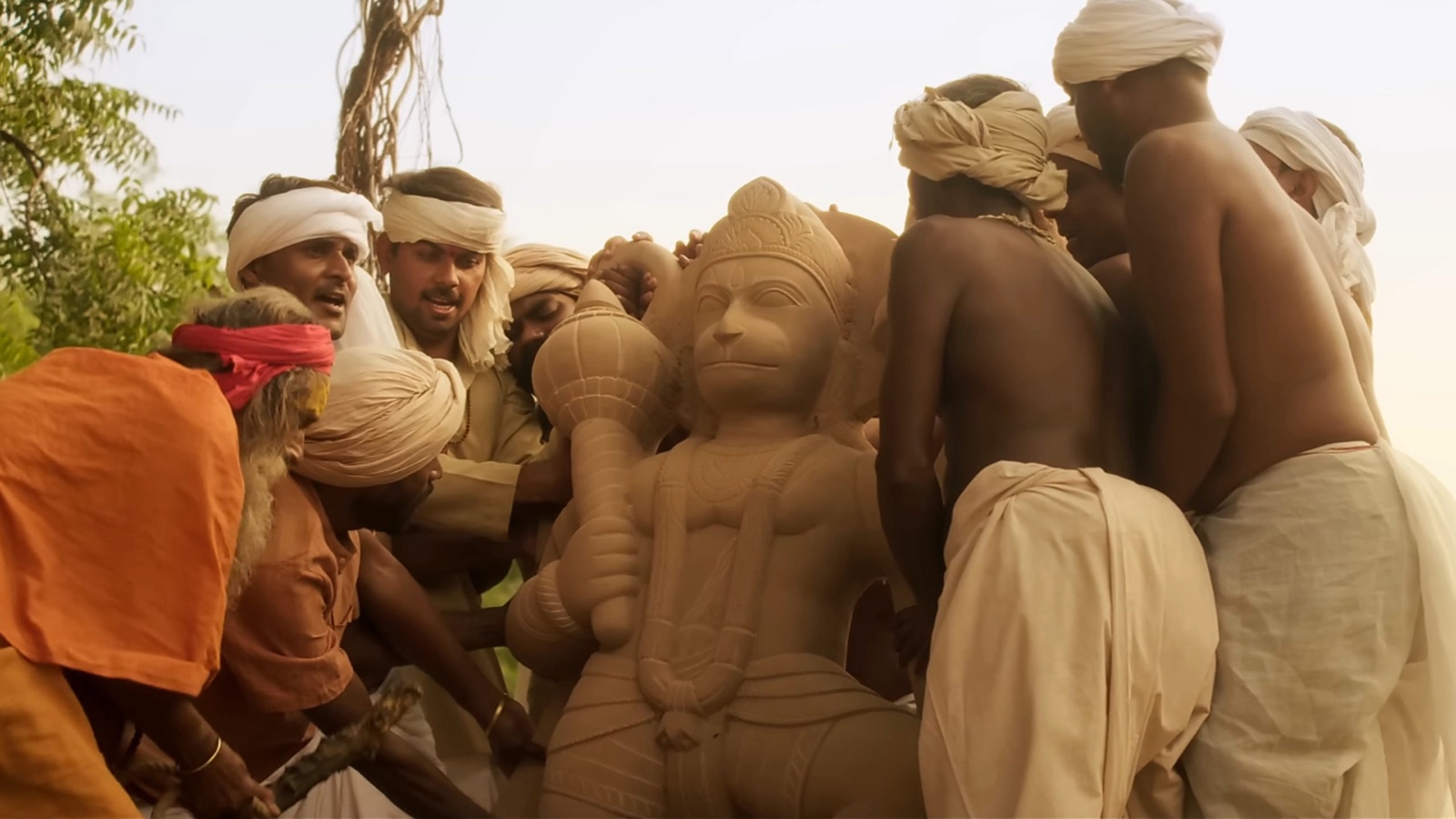 Men in turbans and dhotis carry a stone statue of Hanuman between them