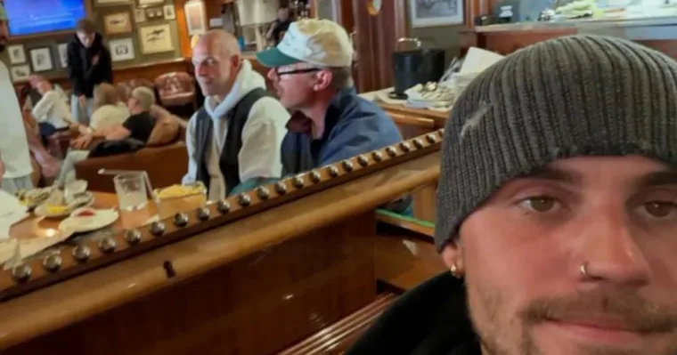Justin Bieber in a grey beanie takes a selfie at a piano, with the restaurant's wooden bar and diners behind him.