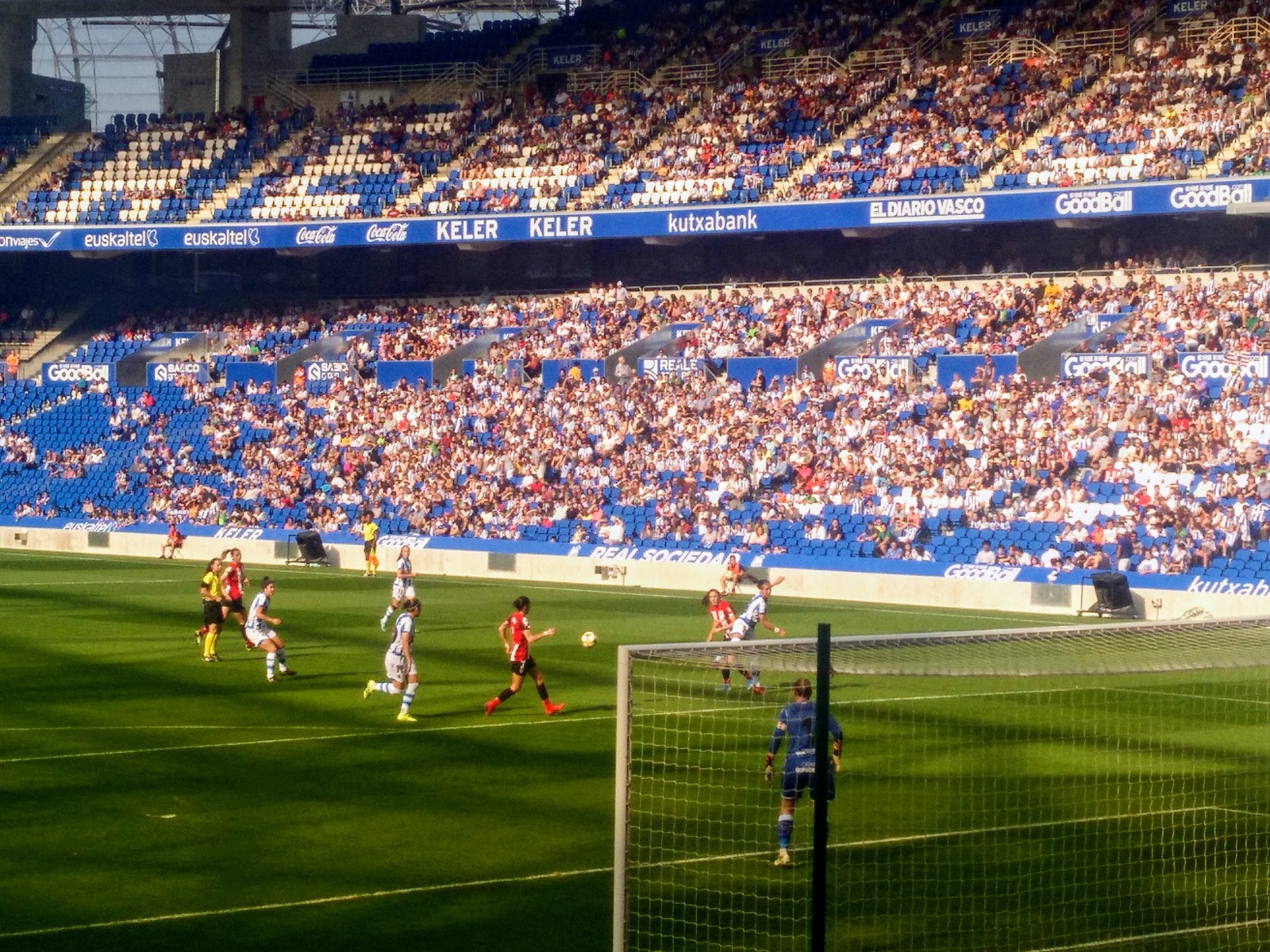 The main stand at the Anoeta in San Sebastián, blue seats packed with Real Sociedad supporters in blue and white, seen from behind a goal during a match