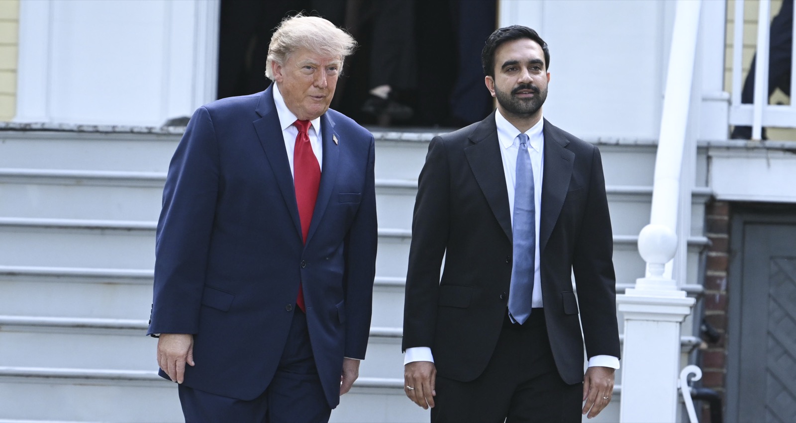 Trump and Mamdani walk down the white wooden steps of the yellow-painted Gracie Mansion side by side, Trump in a navy suit and red tie, Mamdani in a dark suit and blue tie