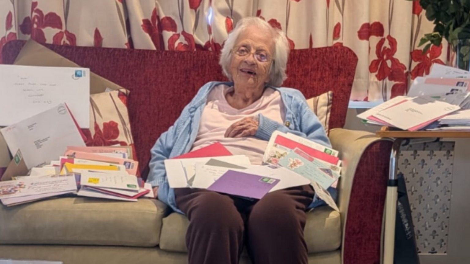 Gwen Chapman sits on a red sofa in a blue cardigan, surrounded by opened birthday cards and envelopes