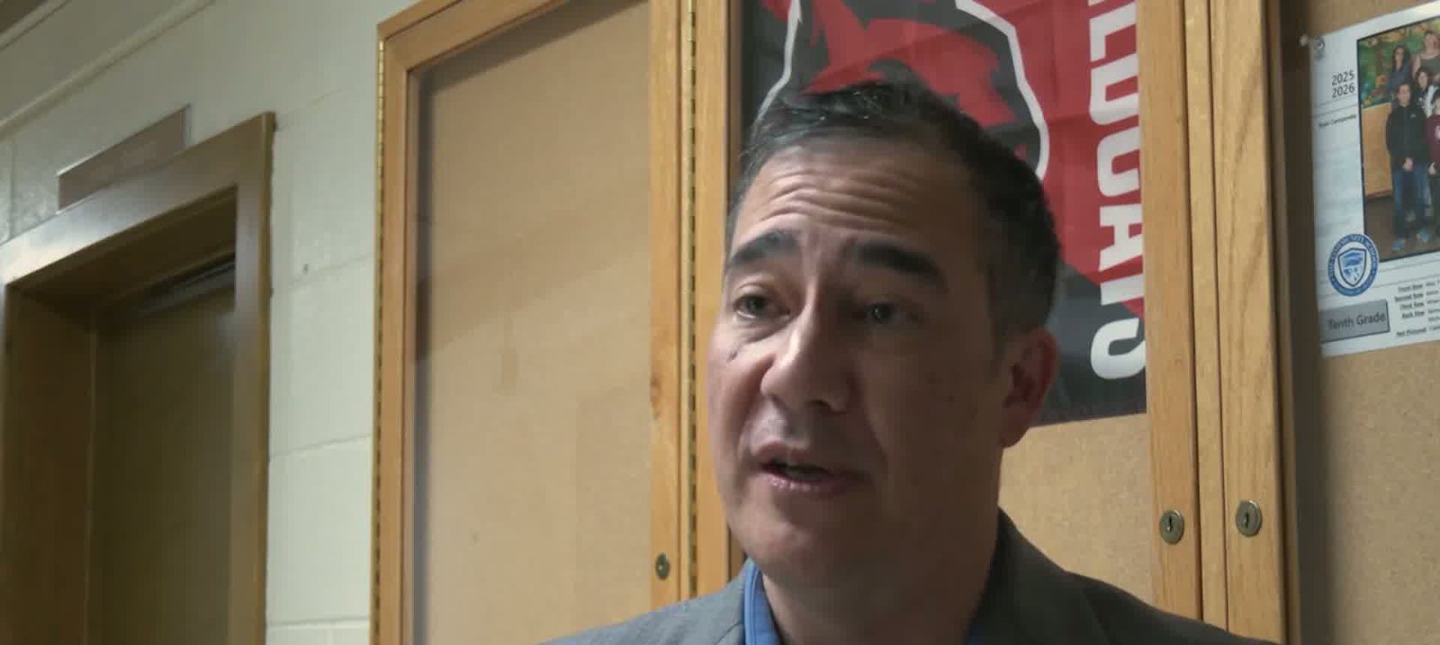 Steve Hobbs in a grey jacket and blue shirt talking to the camera in a school corridor.