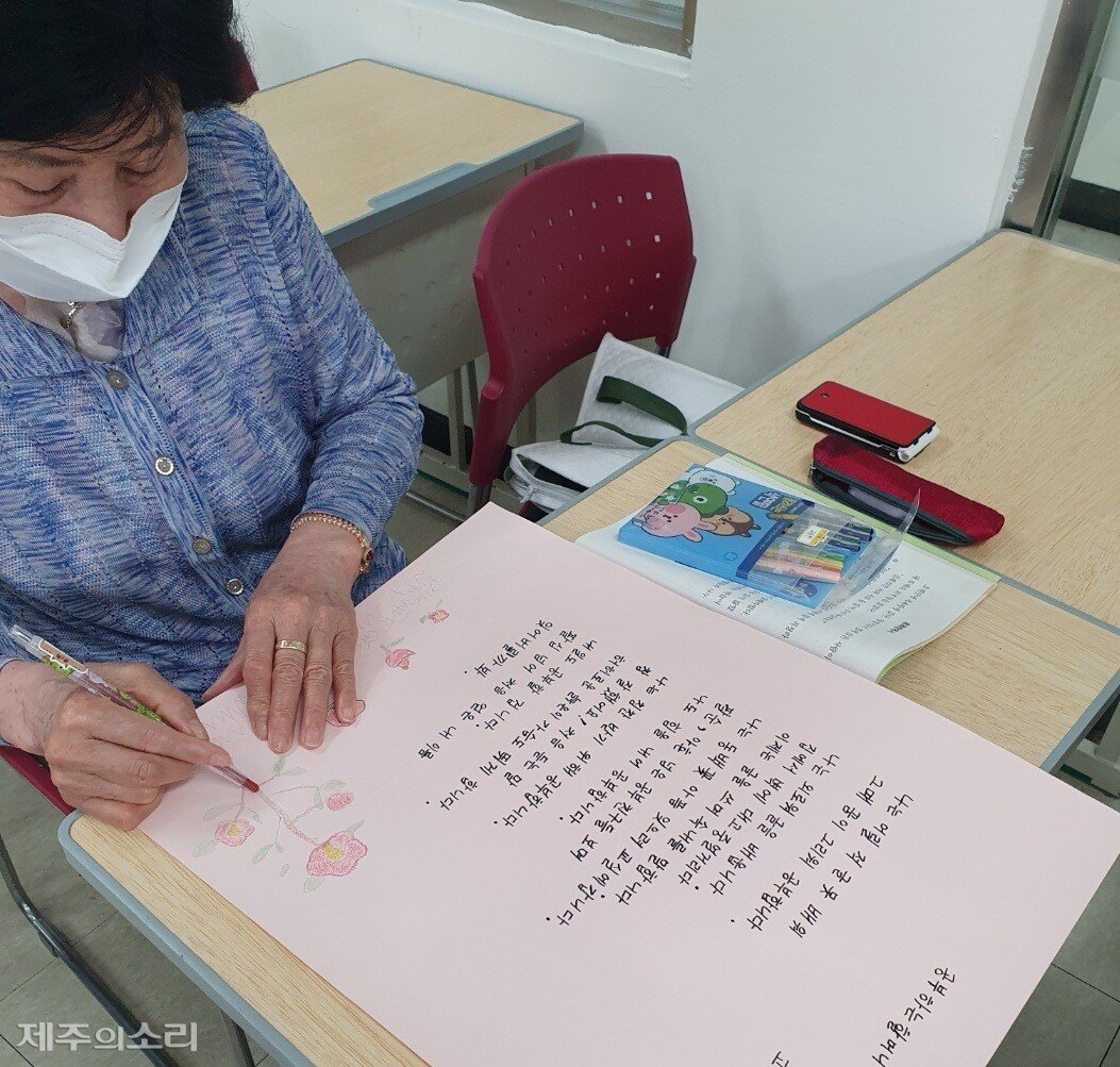An older woman in a mask drawing a red camellia with a coloured pencil beside a handwritten poem.
