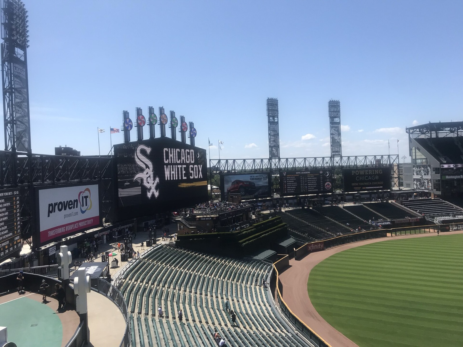 The stands and outfield at the White Sox ballpark on a sunny day, the Chicago White Sox scoreboard above the seats and floodlight towers against a blue sky