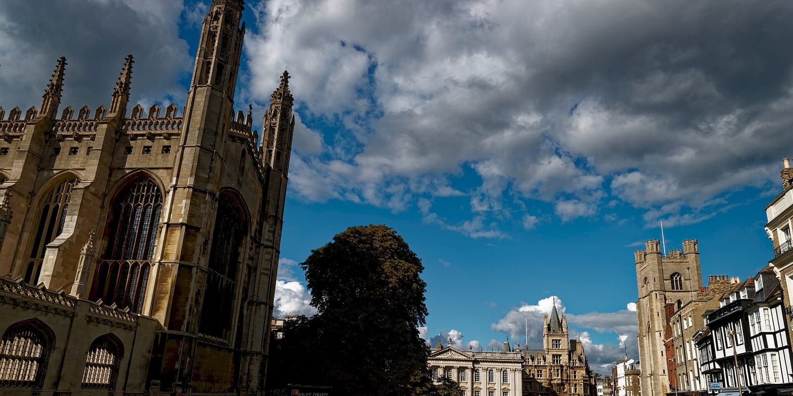 The pinnacles of King’s College Chapel in Cambridge against a blue sky with heavy white clouds, with the Senate House and the tower of Great St Mary’s further down King’s Parade