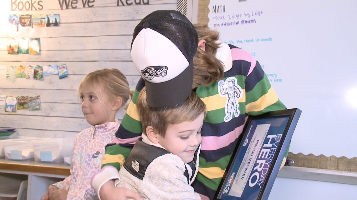 Bryce Rader hugging Major Metzger in a classroom while Major holds a framed Everyday Hero award