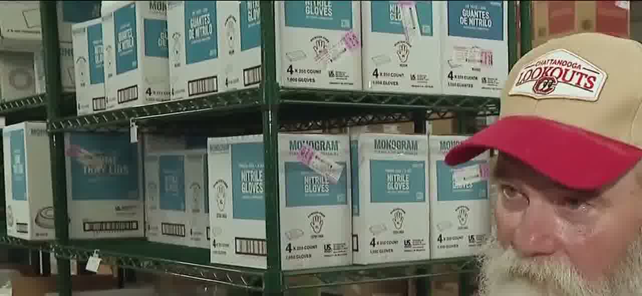 Bob Martin, white-bearded, in a red Lookouts cap and red shirt, talking in the stadium kitchen with shelves of stacked boxes behind him