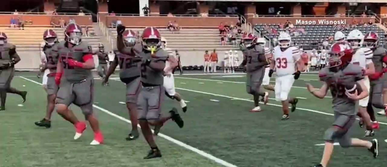Mason Wisnoski running the ball down the right side of the field towards the end zone, teammates in grey ahead of him and Alvin players in white giving chase