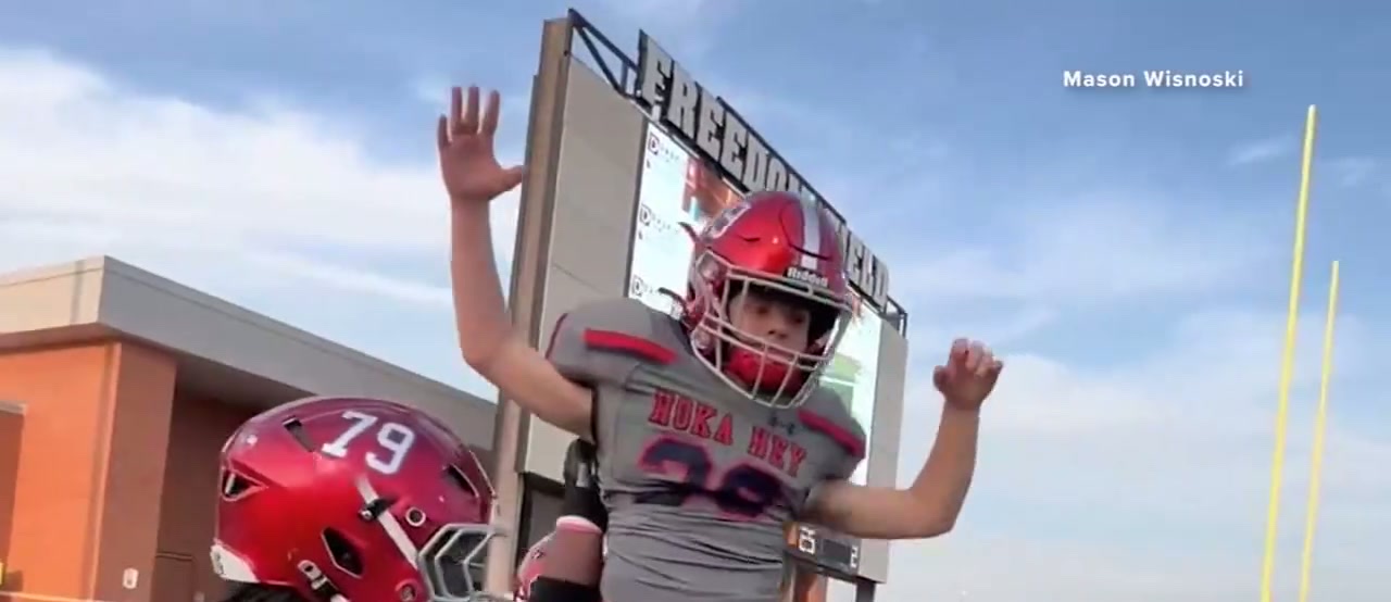 Mason Wisnoski held up on his teammates shoulders with both arms in the air, in front of the Freedom Field scoreboard, another player in a red number 79 helmet below him