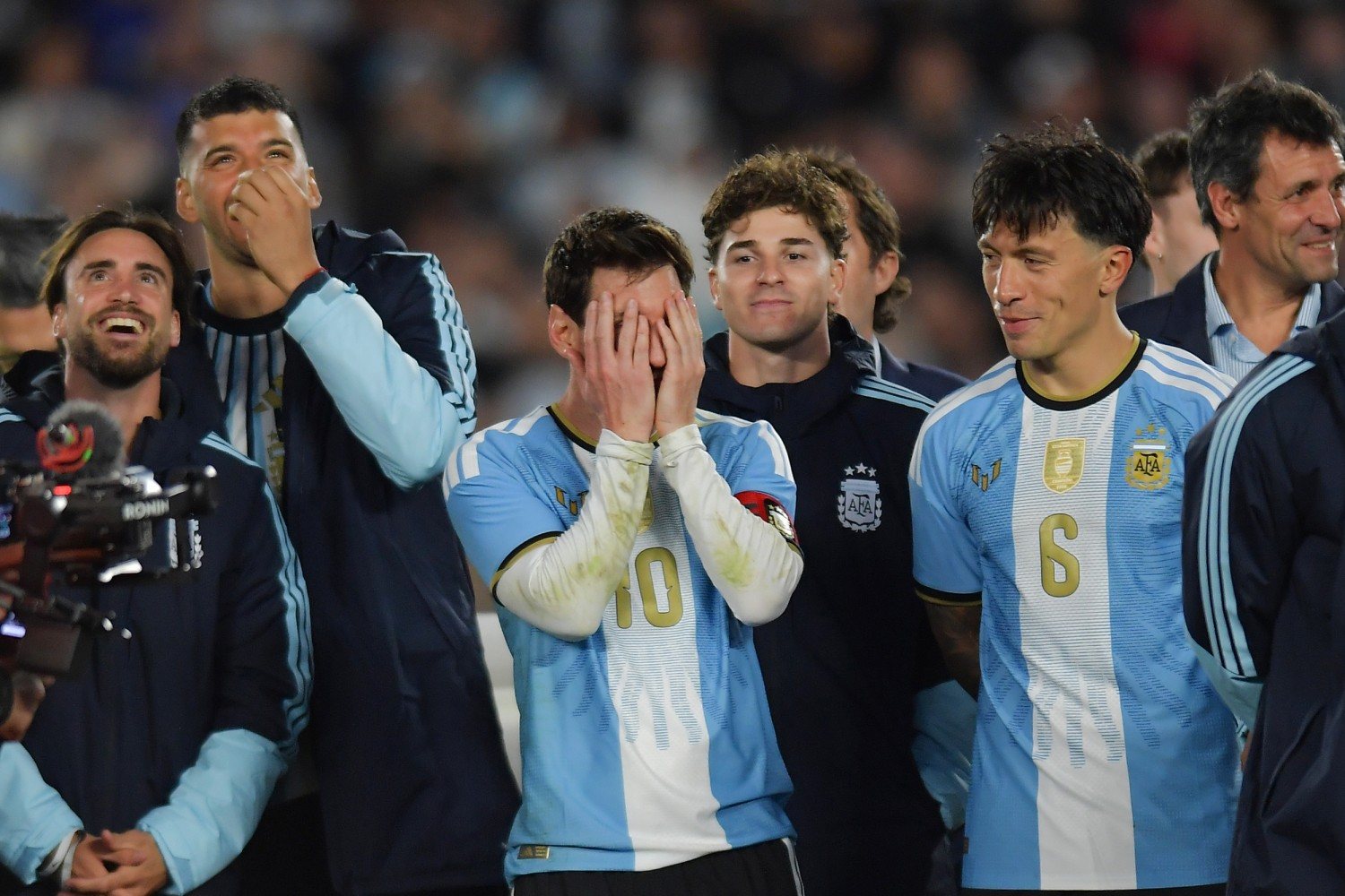 Argentina players in light blue shirts and tracksuit tops watching the sky, one with his hands over his mouth and Messi in the number 10 shirt covering his face with both hands.