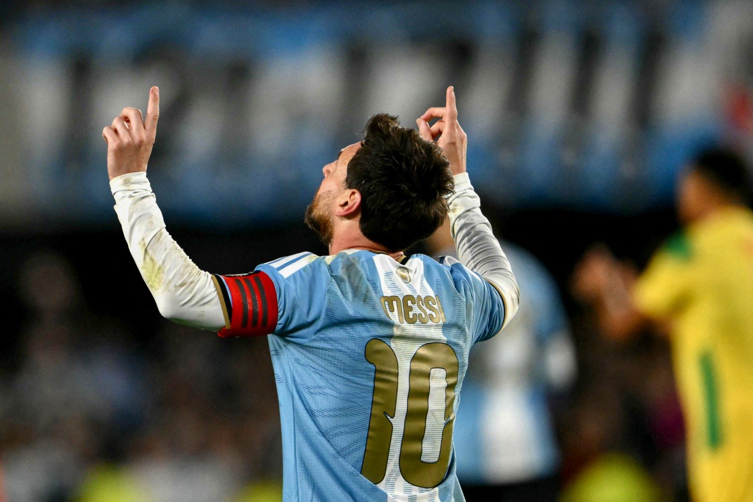 Messi from behind in his number 10 shirt, both index fingers pointing at the sky after scoring.