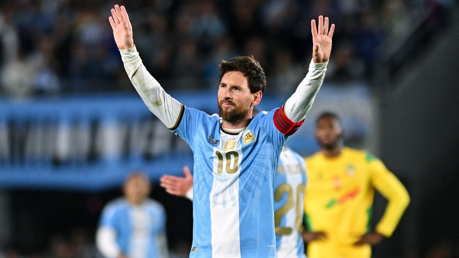 Lionel Messi in the light blue and white Argentina shirt raising both arms to the crowd.