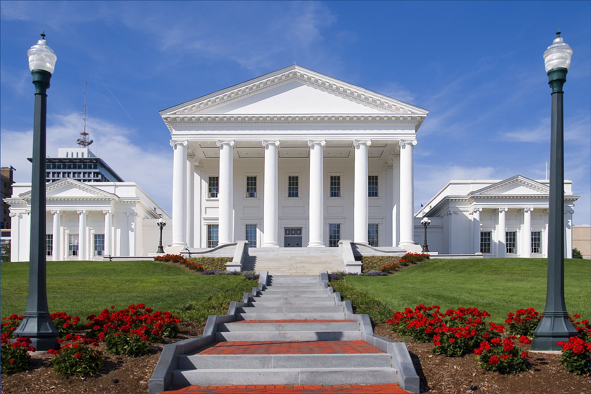 The Virginia State Capitol in Richmond, a white neoclassical building with a columned portico, seen from the foot of a flight of steps with red flowers along both sides