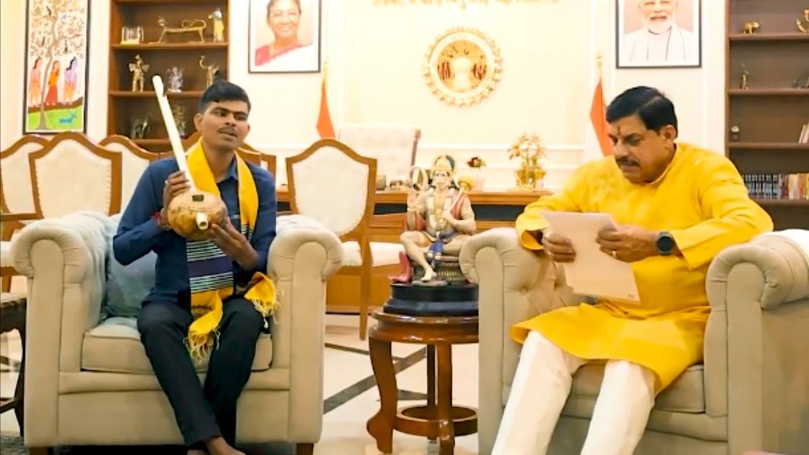 Suneel Lodhi, in a dark shirt with a yellow scarf, holds his tambura on a sofa opposite the chief minister, Mohan Yadav, in the chief minister&rsquo;s residence