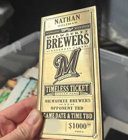 A hand holds a brass ticket engraved Nathan Holzman, Milwaukee Brewers, Timeless Ticket, Miller Park. Below it reads Milwaukee Brewers vs Opponent TBD, Game date and time TBD, $1000.