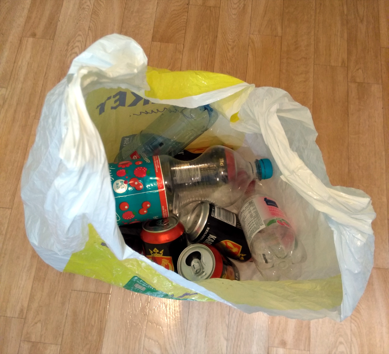 A clear plastic bag stuffed with empty aluminium cans and plastic bottles