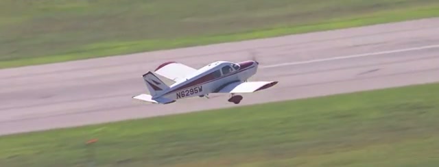 A small white plane with a red stripe lifts off a runway over green grass, seen from above