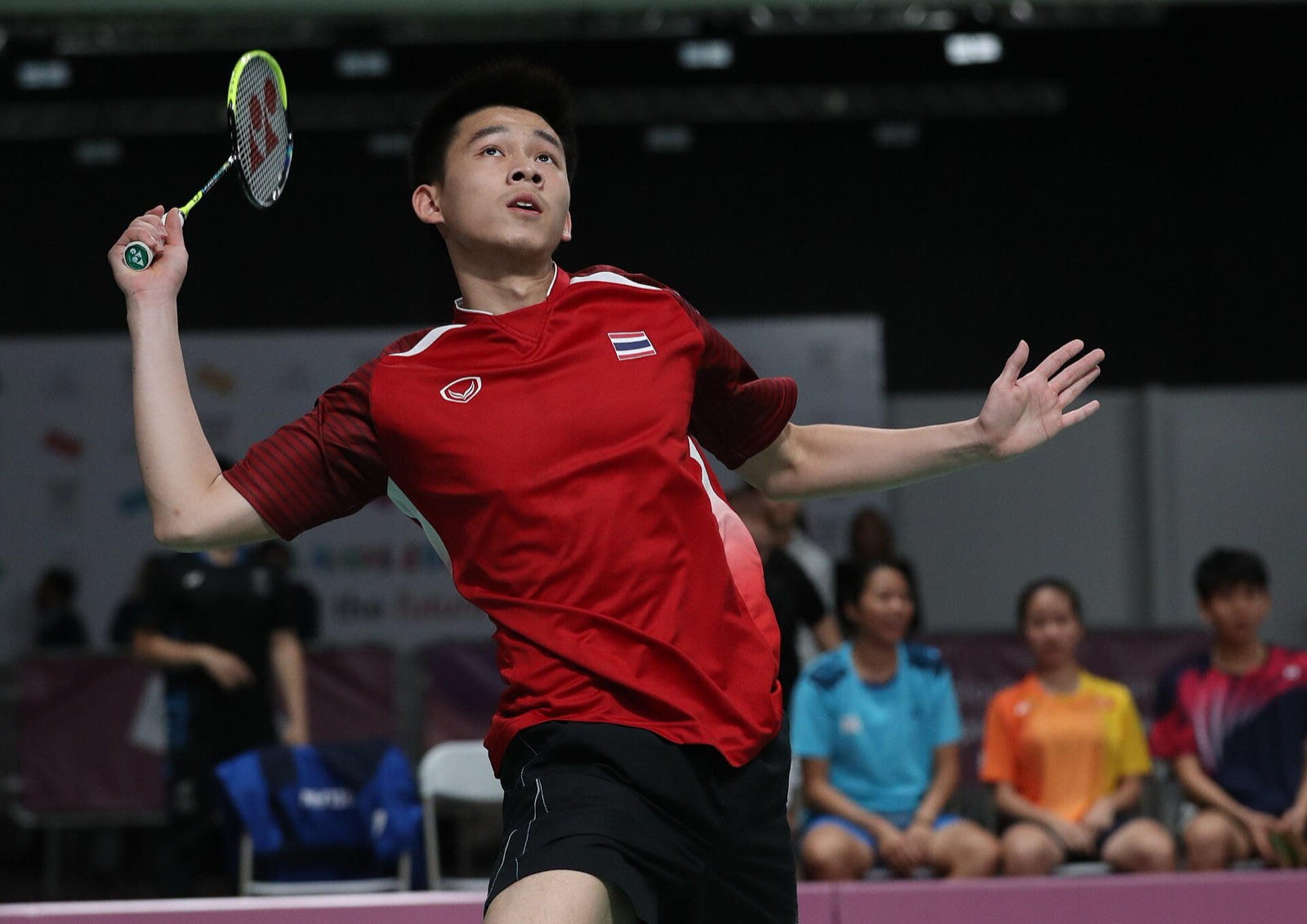 A teenage Kunlavut Vitidsarn in a red Thailand shirt looks up at the shuttle with his racket raised